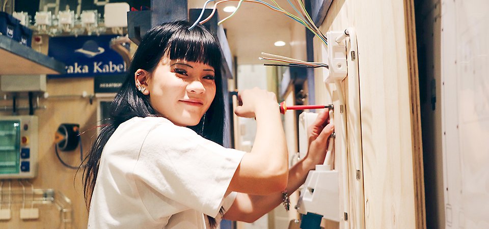 En elev med mörkt långt går använder en mejsel för att arbeta med eltekniska saker.